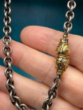 Load image into Gallery viewer, Close-up of a hand holding a silver chain with a gold clasp against a blue background