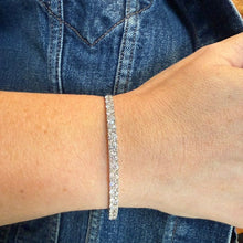 Load image into Gallery viewer, A close-up of a person's wrist wearing a slim, sparkling silver-toned bracelet, with blue denim clothing in the background.
