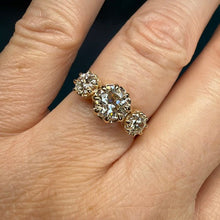 Load image into Gallery viewer, A close-up of a hand wearing a yellow gold ring with three round-cut clear gemstones in a row.
